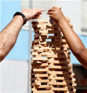 Zwei unterschiedliche Hände bauen gemeinsam an einem Turm aus Holzklötzchen